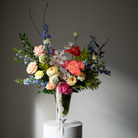 A large, colourful arrangement in a footed vase with trailing flowers.