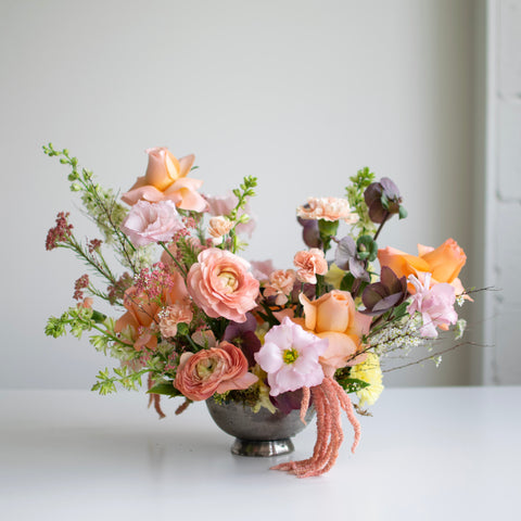 Beautiful arranageent with peach, orange and pink palette with accents of purple and greenery. 