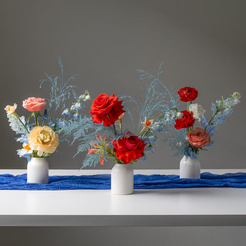 Three bud arrangements in white vases sit together on a grey background.