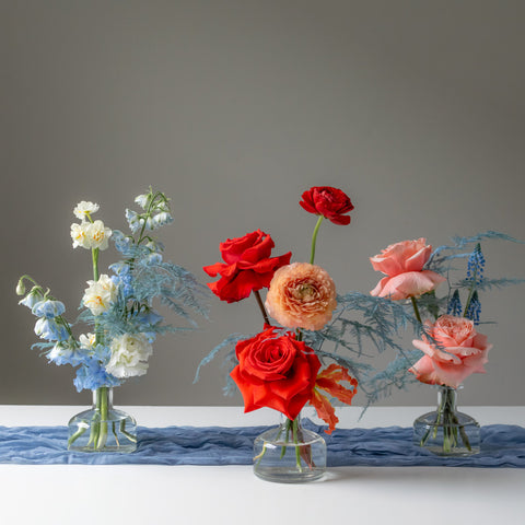 Three mini floral arrangements sit in glass bud vases. 