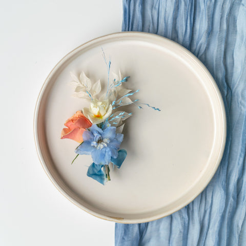 A blue, white and orange boutonniere sits against a white plate