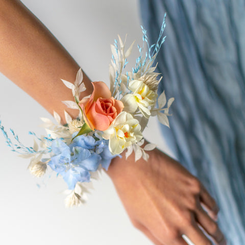 A predominantly white corsage with pops of peach and blue fresh flowers.
