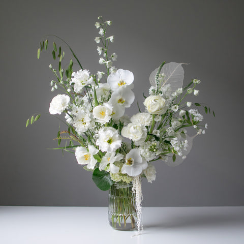 Elegant all white arrangement in a glass vase with added greenery. 