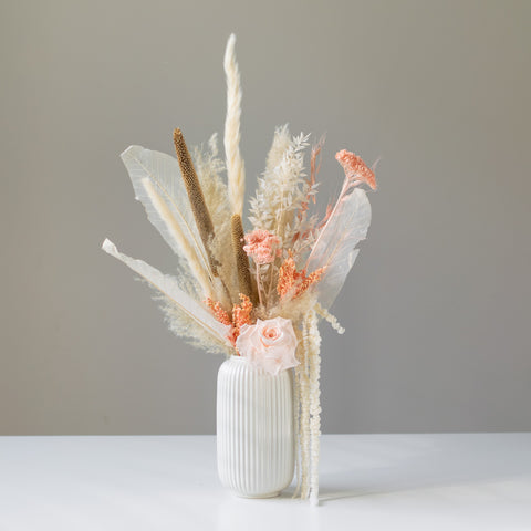 Elegant dried arrangement in a off-white textured ceramic vase. Has a muted neurtral colour palette (crema,s browns, and peach accents)