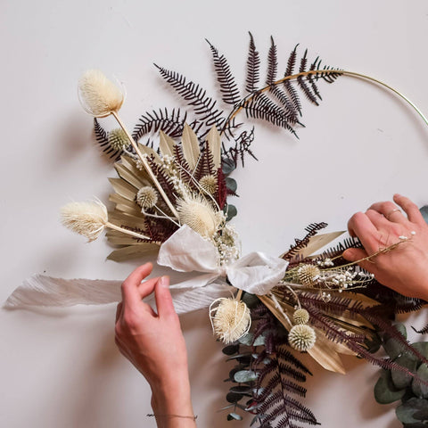 Two hands reach into frame to make adjustments on a dried wreath.