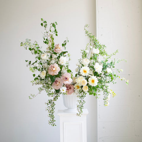 A large sympathy arrangement with light pink accents sits on a white pedestal.