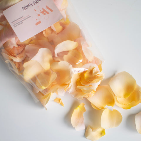 A clear bag full of cream rose petals are spilling out onto a white table.