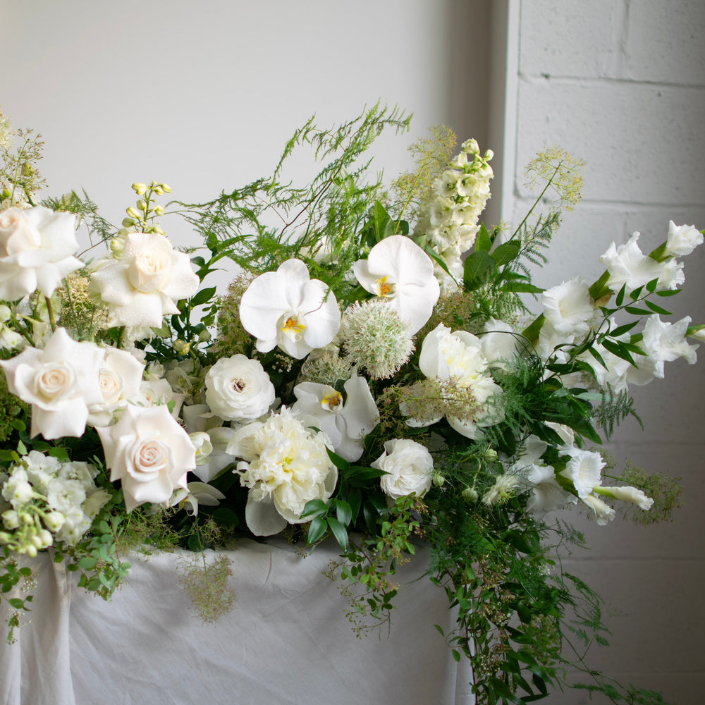 A traditional white and green casket spray with cascading greenery.