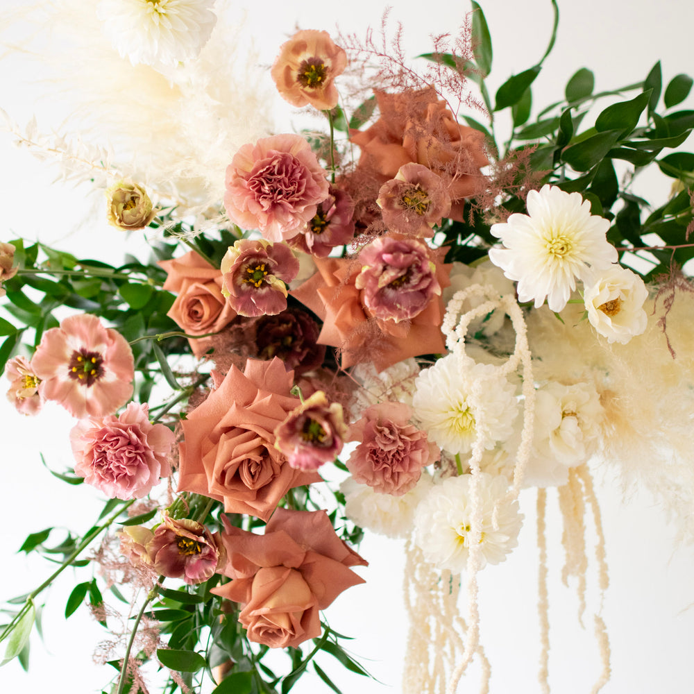 A close-up of muted pink carnations and roses flanked by white trailing flowers and dahlias.