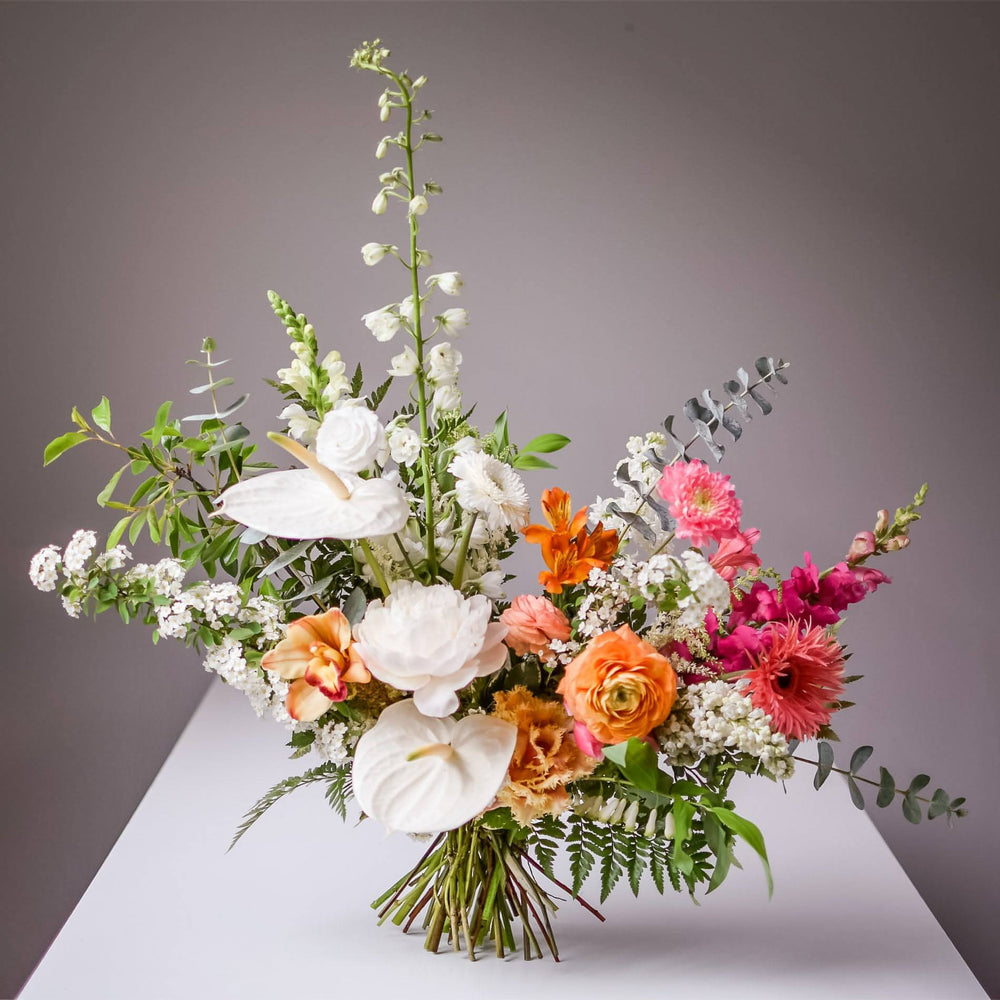 A bright white bouquet with pink and orange accent flowers. Anthurium and eucalyptus are used.