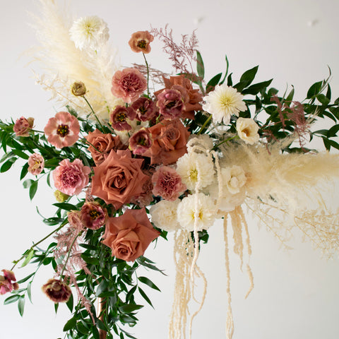 Dark, muted blush roses and cream coloured flowers drape across the top left corner of a simple arch.