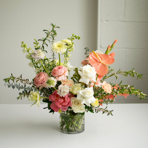 An elegant flower arrangement with pink, peach, and cream coloured blooms.
