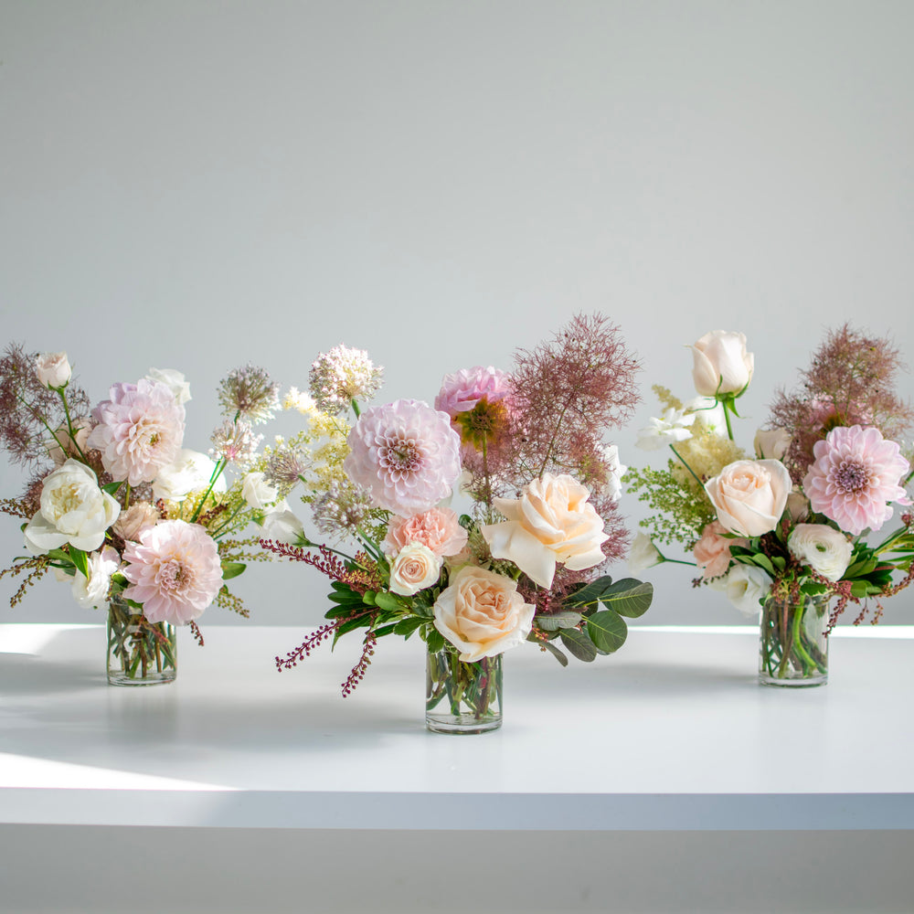 Three mini floral centrepiece in glass vases. The color palette is soft blush tones.