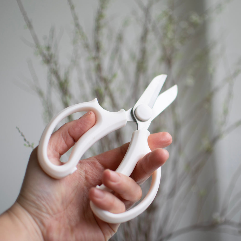 Metal flower shears being help in front of flowering branches.