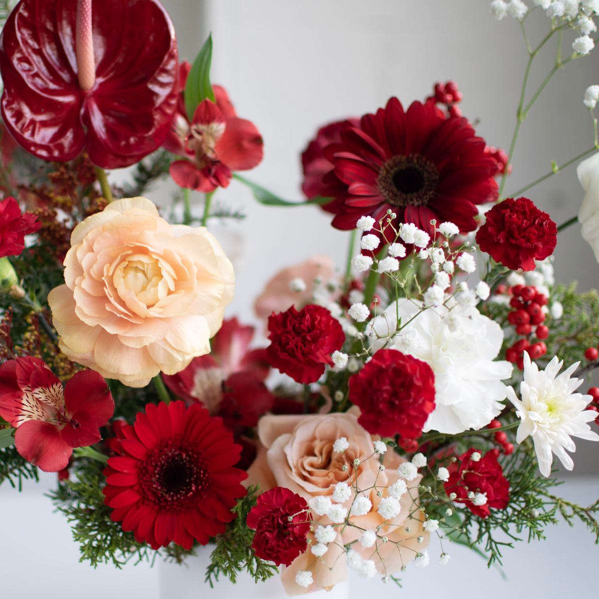 Red, peach and white festive flowers in a white ceramic vase.