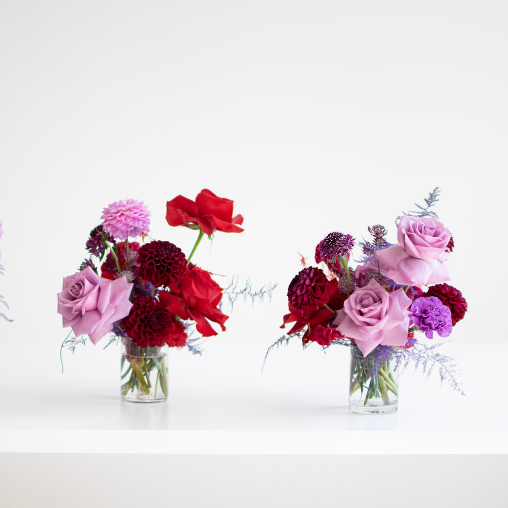 Red and purple flowers are arranged in glass vases. Lilac roses and deep red dahlias.