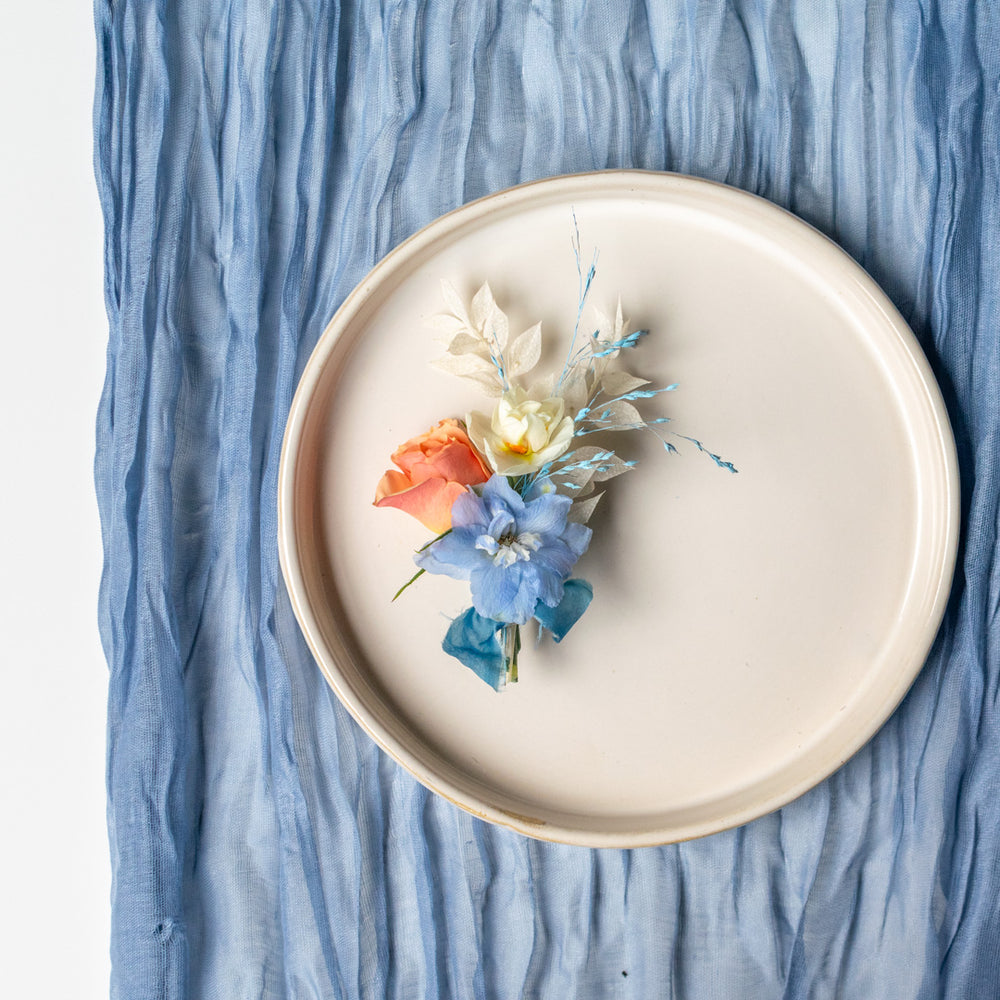 A blue, white and orange boutonniere sits on a white plate against a blue cloth
