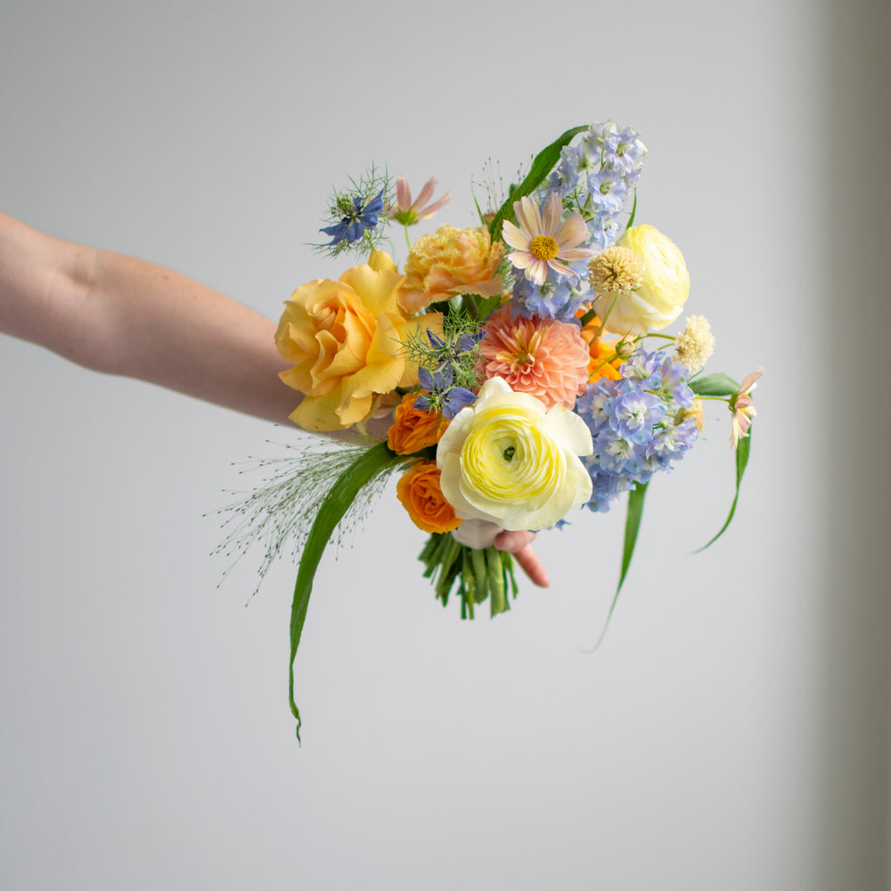 A spring-themed bridesmaid bouquet, with light yellows, oranges, pinks, and blues.
