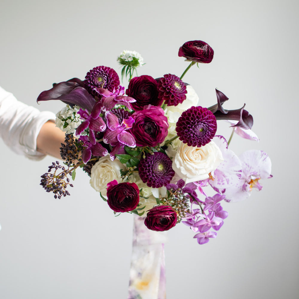 A large bouquet with lots of deep purple dahlias and ranunculus, accented with white roses.
