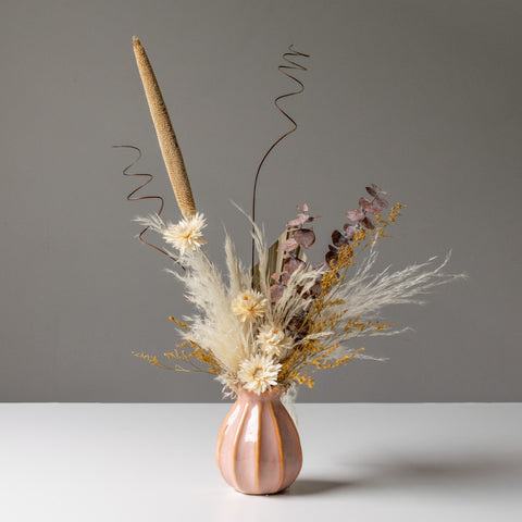 A muted pink and beige dried floral arrangement in a geometric pink vase.