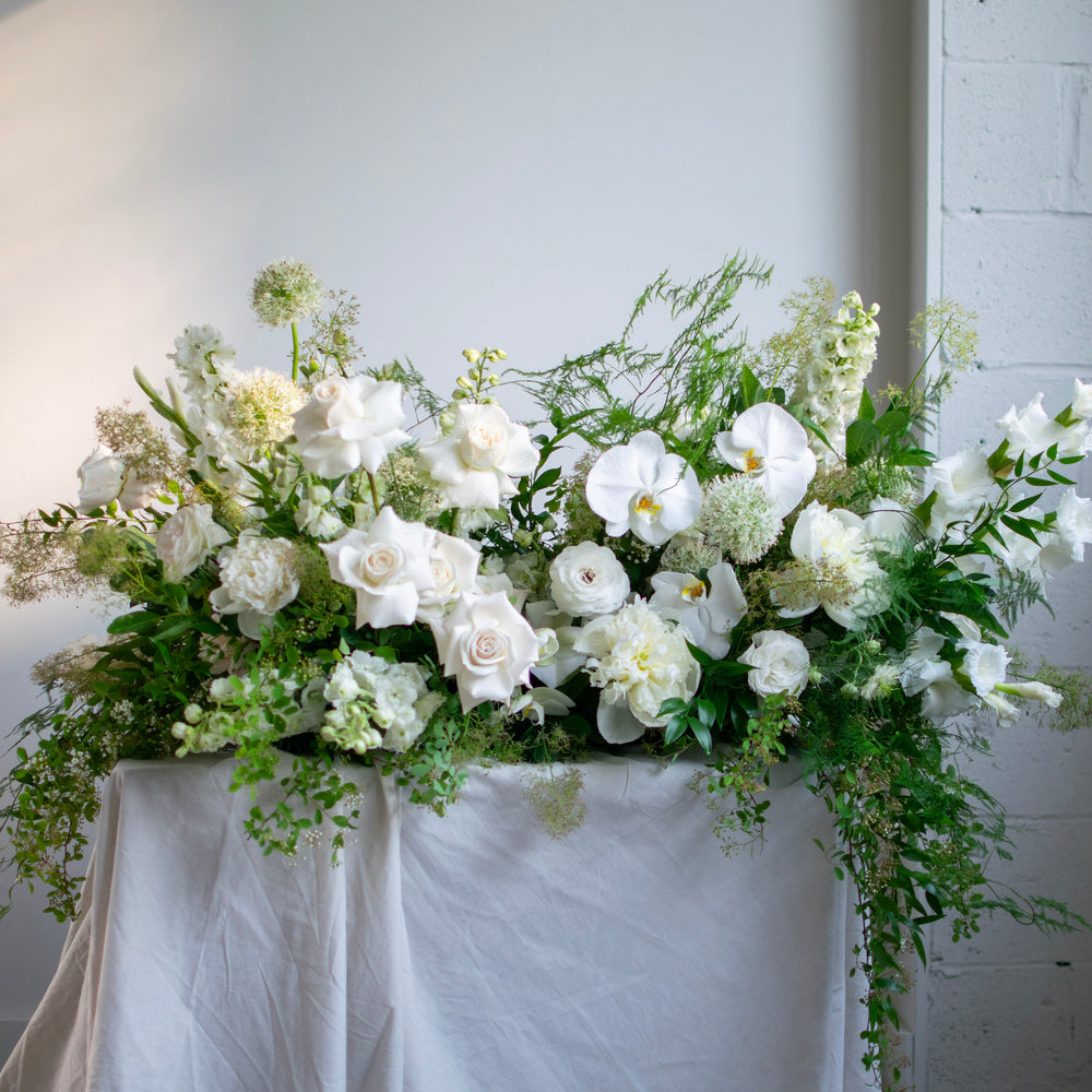 A luxurious white casket spray made with lots of fresh greenery.