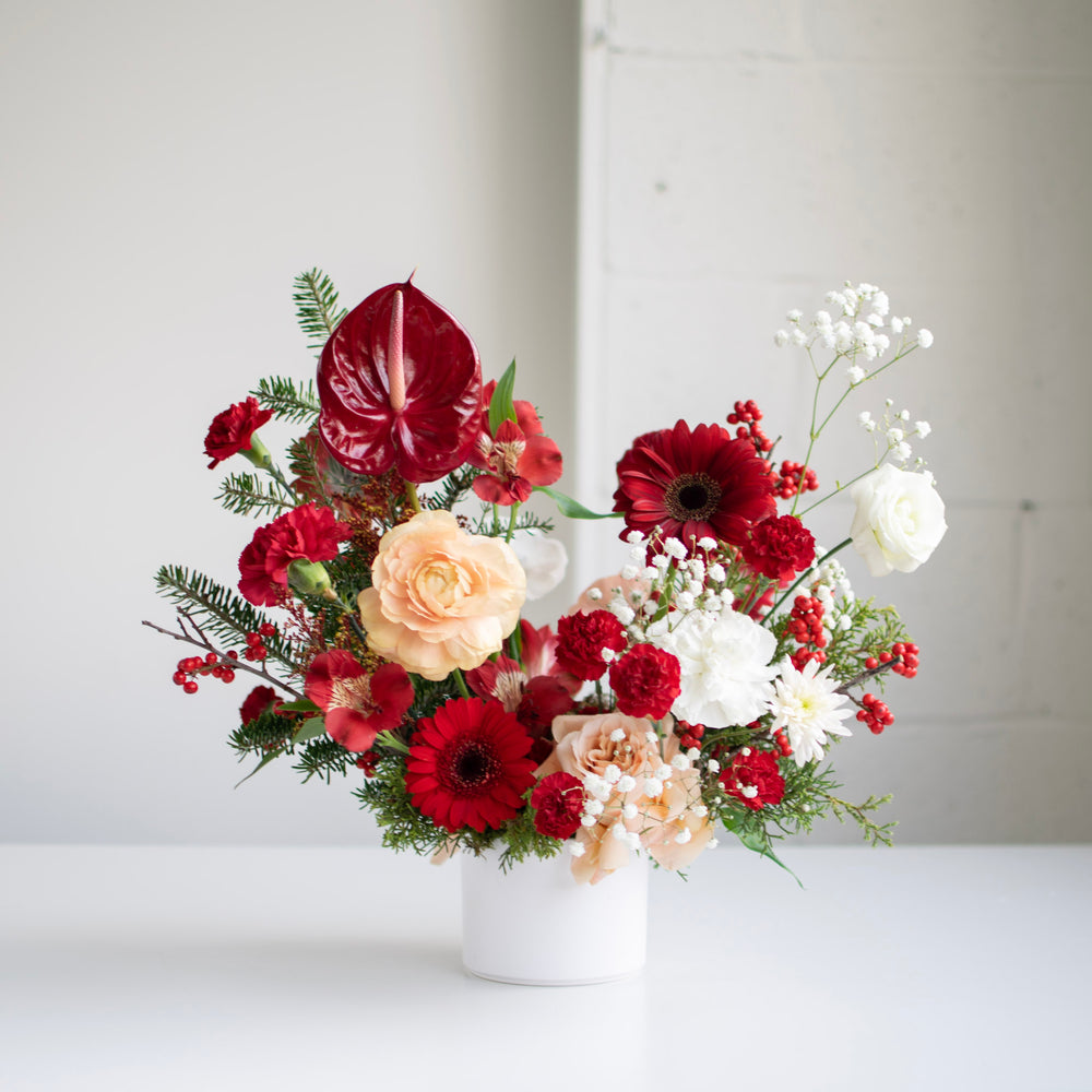 Red, peach and white festive flowers in a white ceramic vase.
