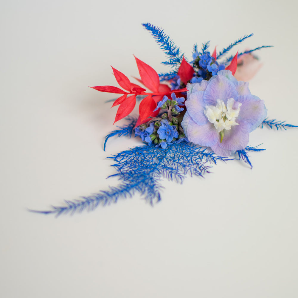 A top view of a dyed, fresh floral boutonniere in blue and red.