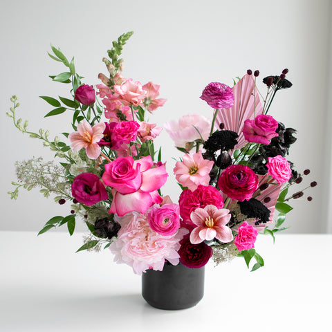Romantic hot pink flowers with red and black accents in a black cylindrical vase.
