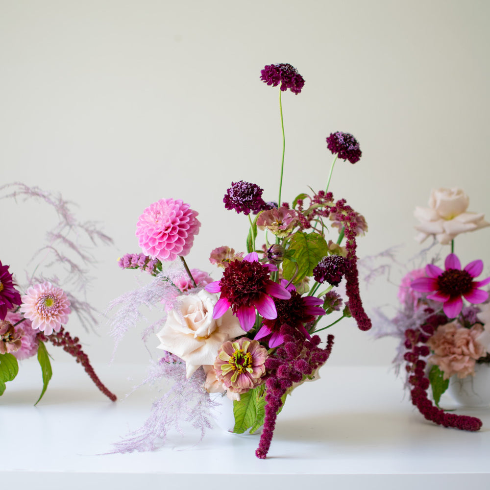 A row of small flower arrangements in pink and purple jewel tones.