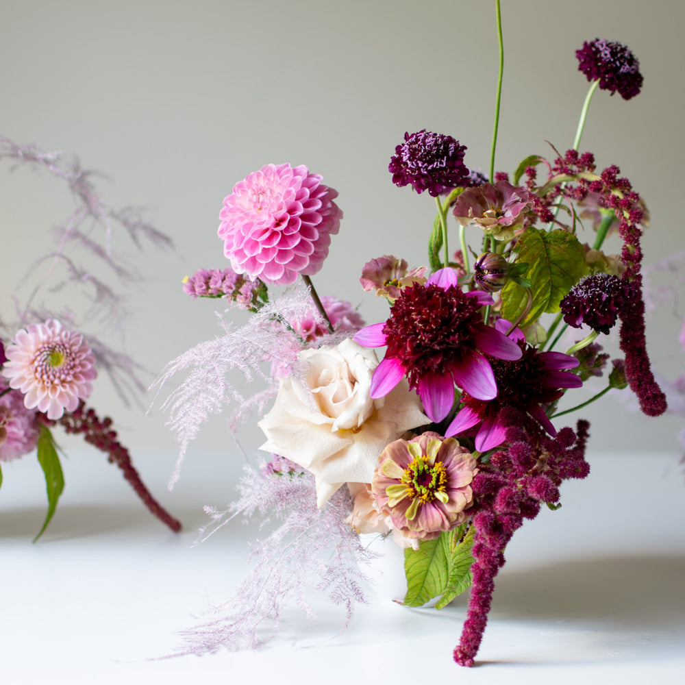 A mini purple flower arrangement in a small white vase.