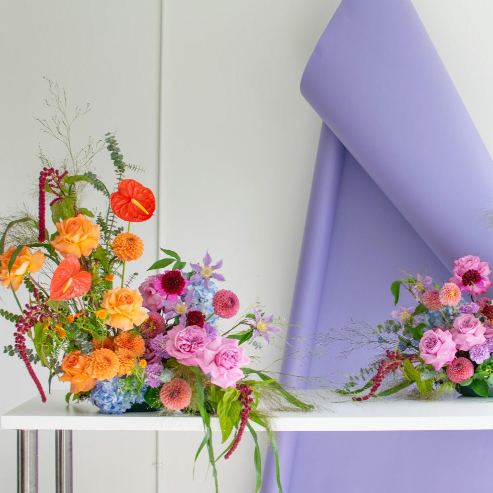 Two fresh flower arrangements sit on a white table. They both have pink roses.