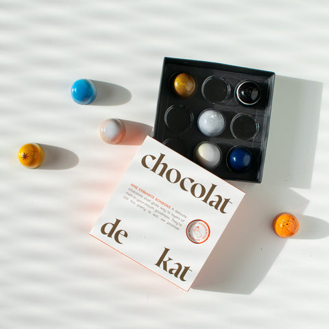 Chocolat de Kat chocolate truffles are scattered around a simplistic, square white box.