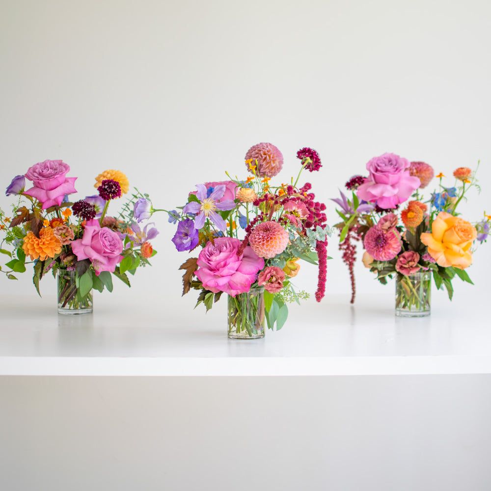 Three small flower arrangements made with bright pink flowers and orange accents.
