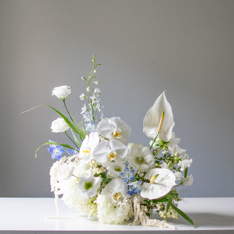 Orchids and anthuriums are used in a white wedding arrangement with hints of light blue.