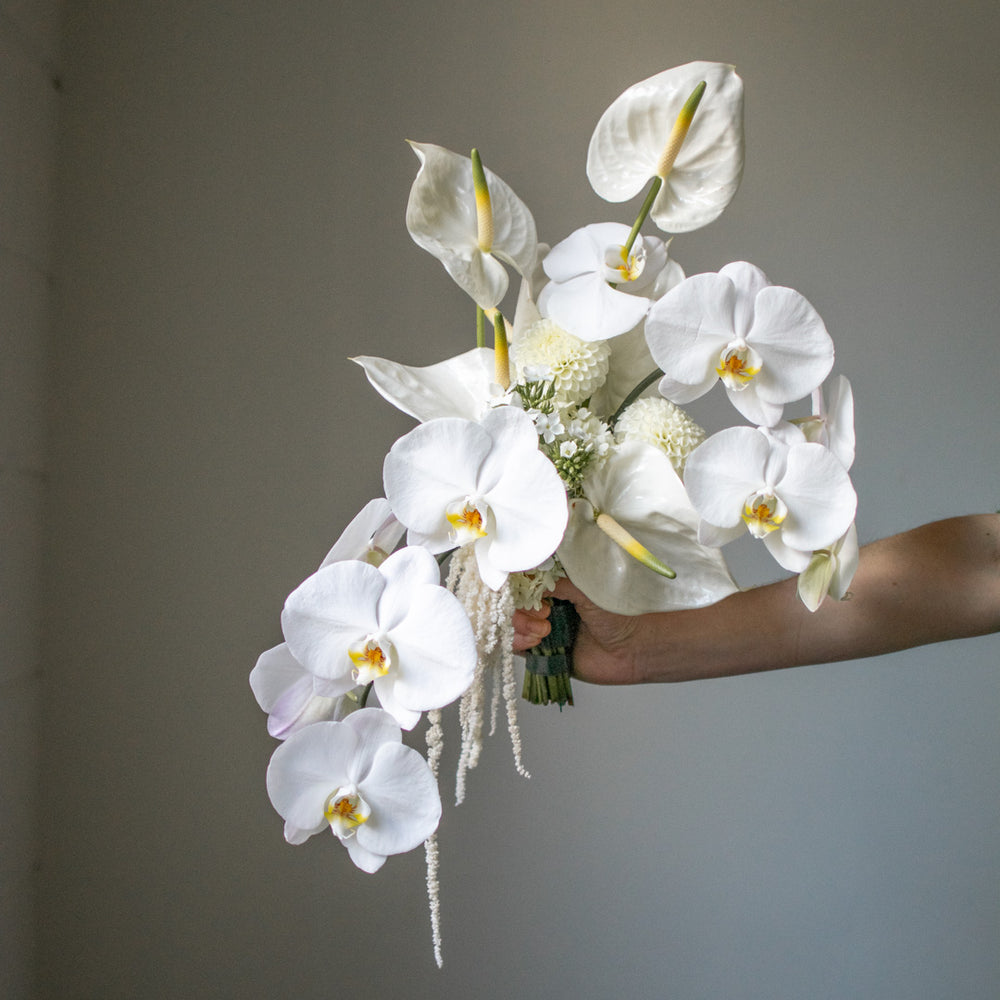 A custom made bridal bouquet with minimal greenery containing anthurium, orchids, dahlias, and trailing flowers.
