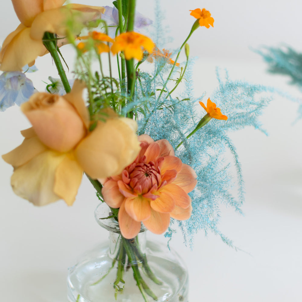 A close up of muted orange flowers in a glass bud vase.