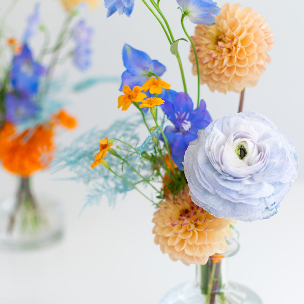 A close up of a baby blue ranunculus and peachy dahlias in a floral arrangement. 