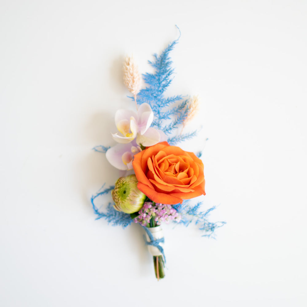 A bright orange rose is the centrepiece to blue and white accents in a groom's boutonniere.