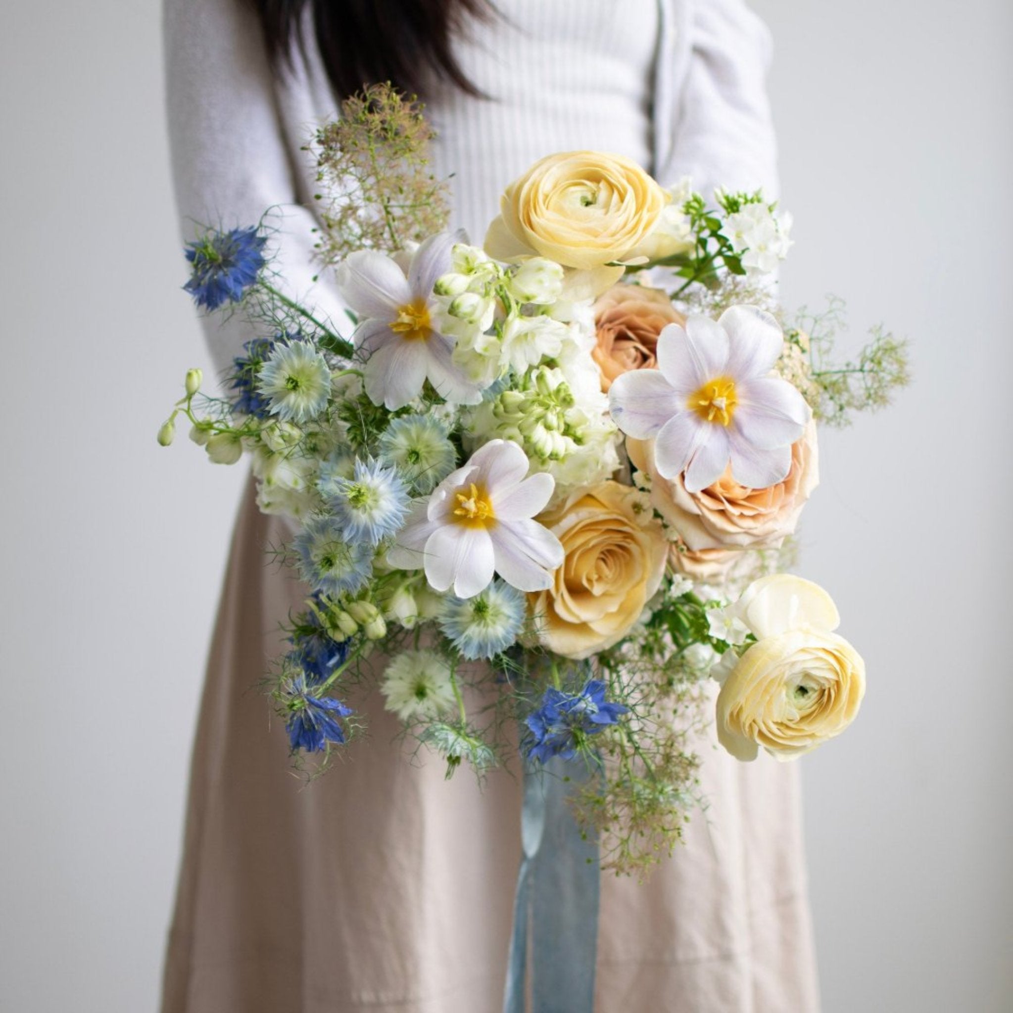 A woman holds a wedding bouquet against her torso. A silky blue ribbon trails from the stems.