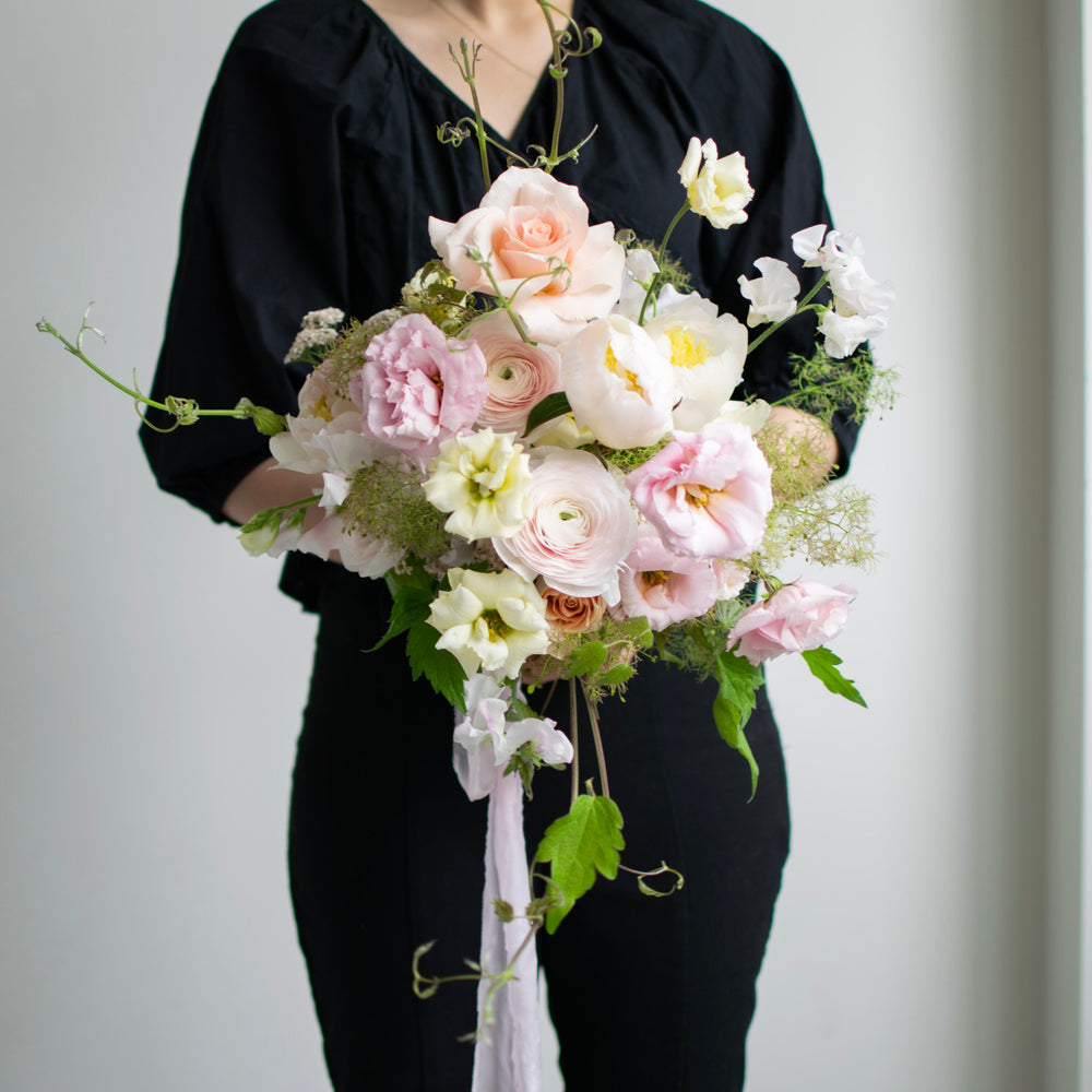 A woman dressed in all black holds a soft pink bouquet. There is lots of trailing greenery.