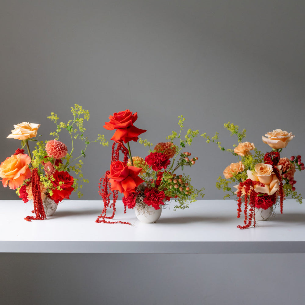 Three red floral arrangements with peach and green accents in small white vases.