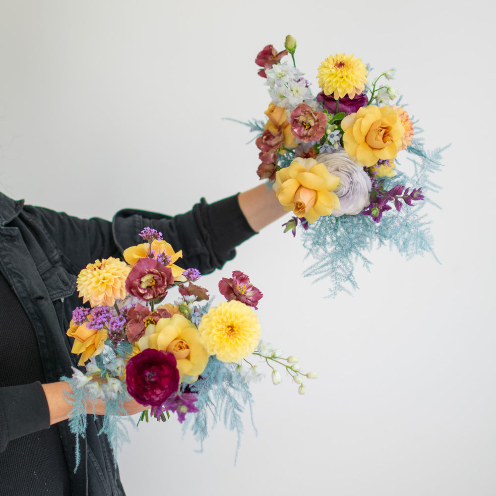 A person holds two small bouquets in their hands. The flowers are light and colourful.