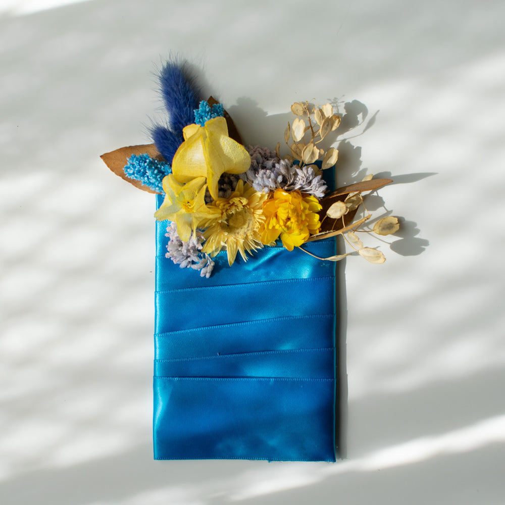 A pocket boutonniere made with dried florals. The palette is yellow and blue.