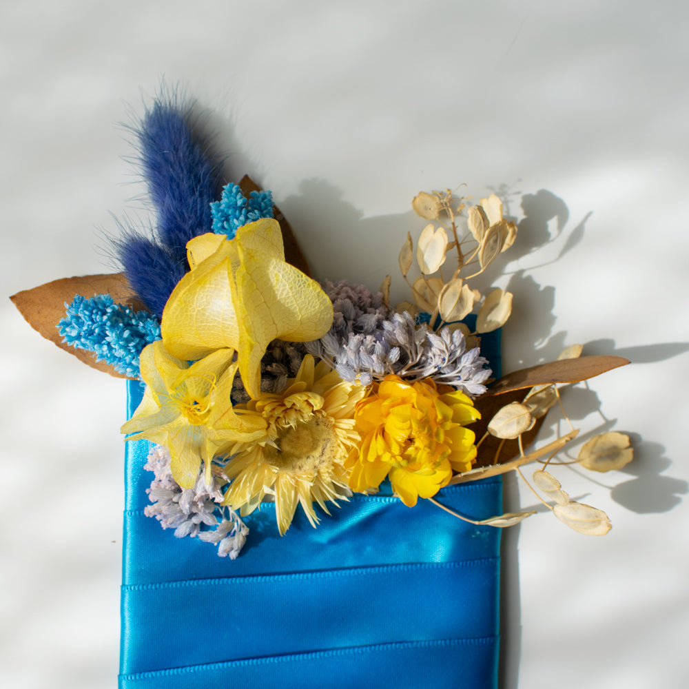 Dried yellow flowers on a boutonniere are contrasted with dyed blue bunny tails. 