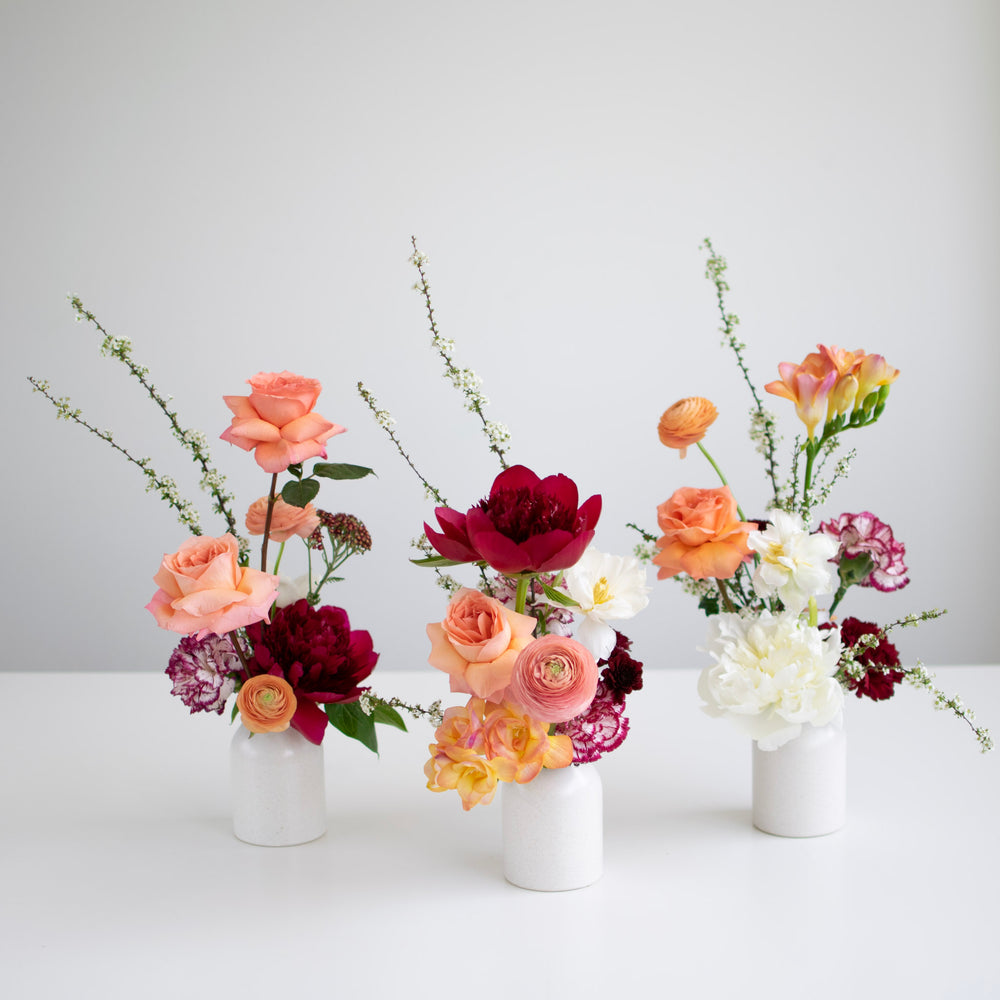 Three bud arrangements in white vases sit together on a white background.