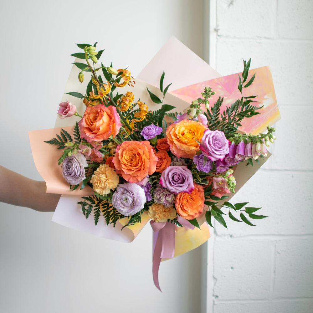 A cheerful bouquet of flowers with purples and pinks, wrapped in decorative paper.