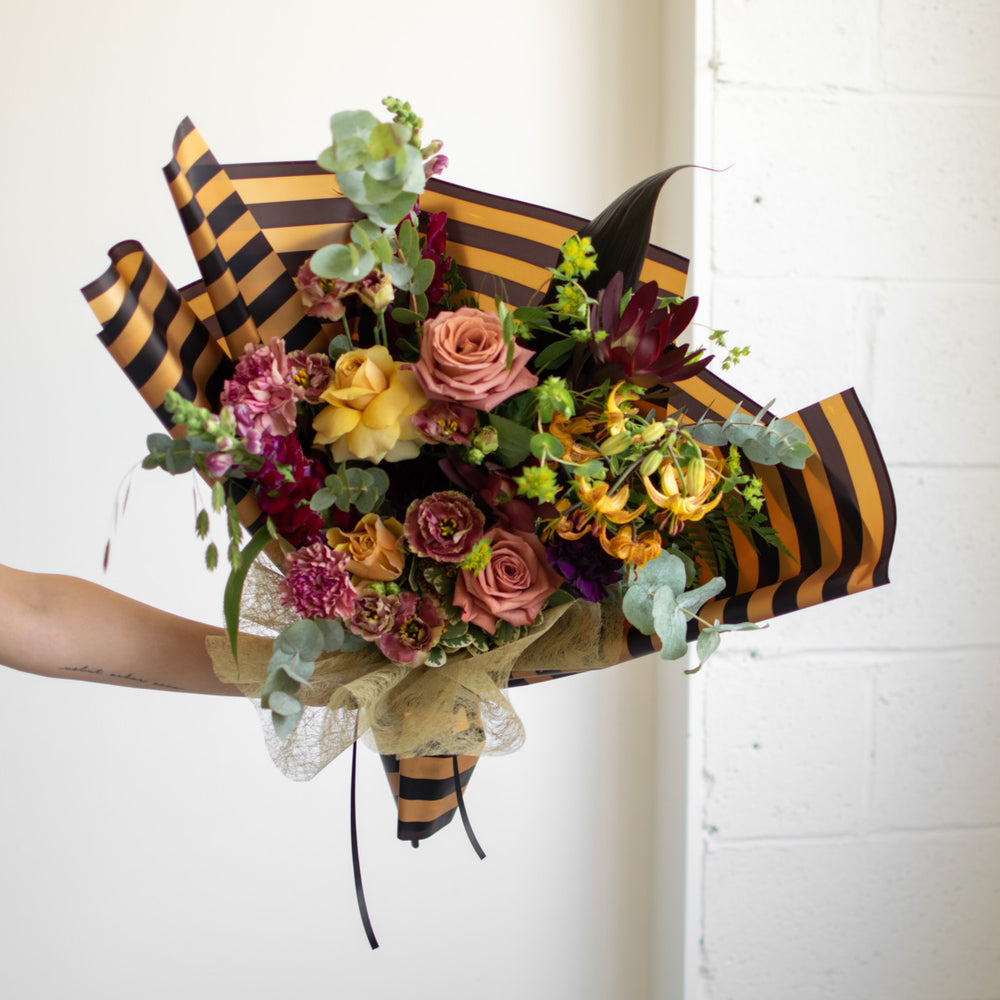 A moody flower bouquet with lots of roses. It is decoratively wrapped in complementary paper..