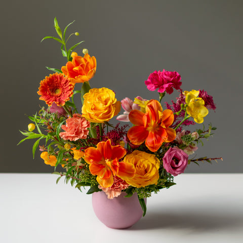 A fresh floral arrangement with pinks, yellows, and oranges in a pink ceramic vase