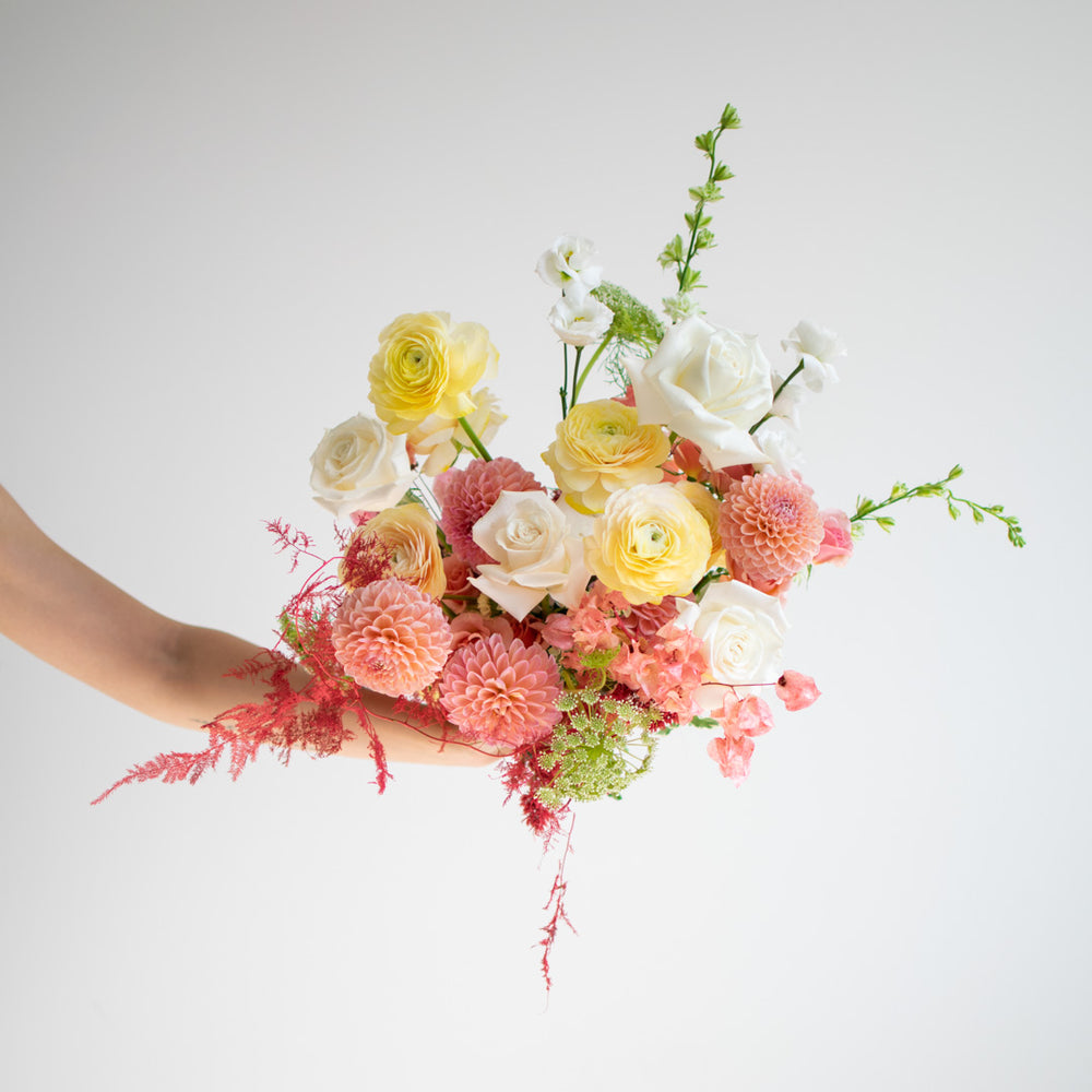 A pastel bouquet made of light pinks, yellows, and white roses.