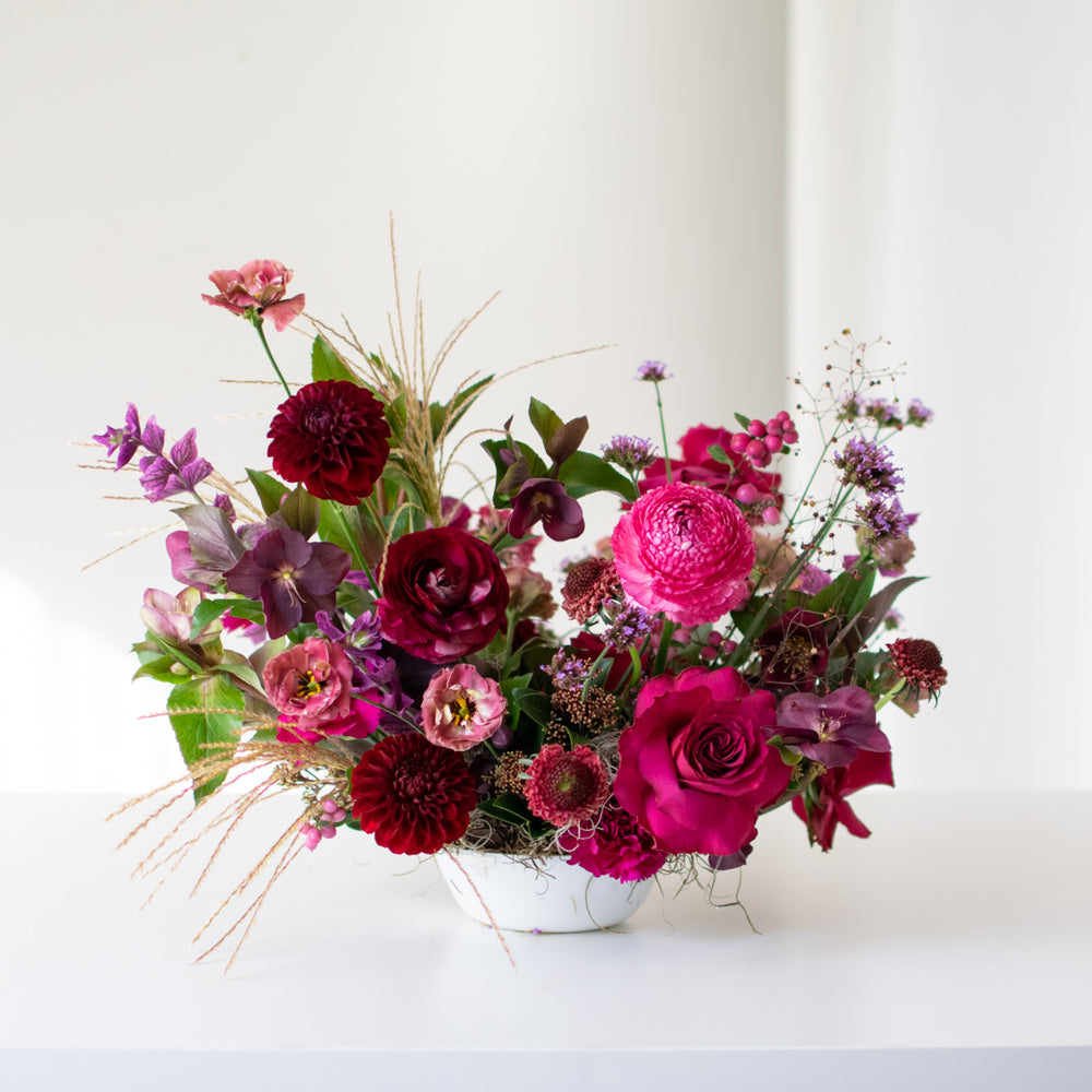 A deep pink and purple jewel toned centrepiece in a white bowl. 